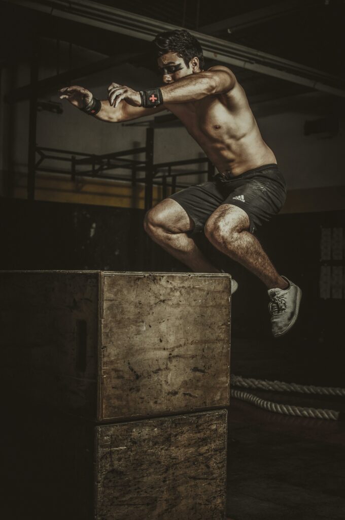 pexels-photo-9602280-9602280 Shirtless man performing a high-intensity box jump exercise in a dimly lit gym.